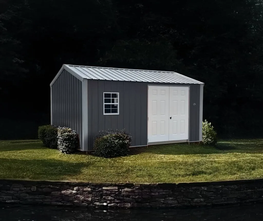 Gray Classic Garden Shed with white trim and double doors displayed on a landscaped lawn near water