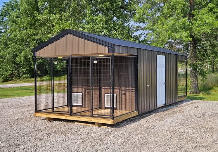 Brown dog kennel with black trim, double outdoor runs, and side entry door on a gravel lot