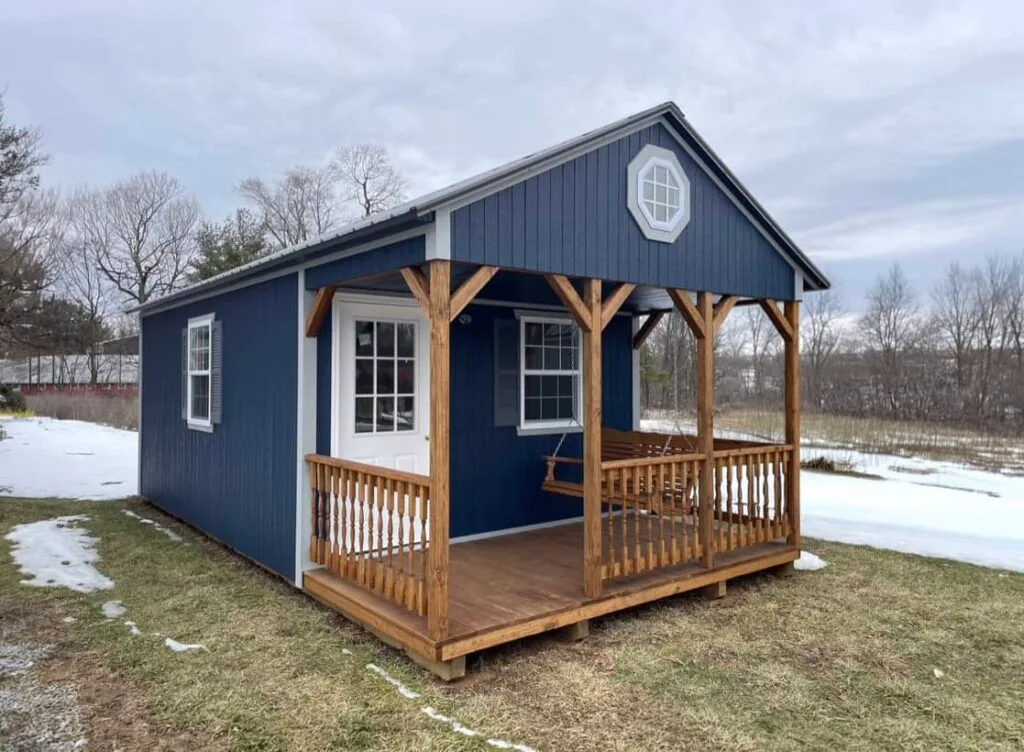 Blue Elite A-Frame Cabin with white trim, covered front porch, and octagon gable window in a winter landscape