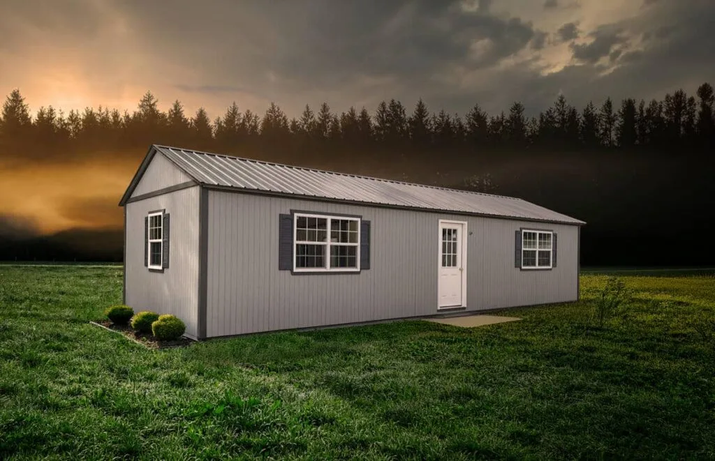 Light gray Elite Cabin with white trim, side entry door, and multiple windows in an open field at sunset
