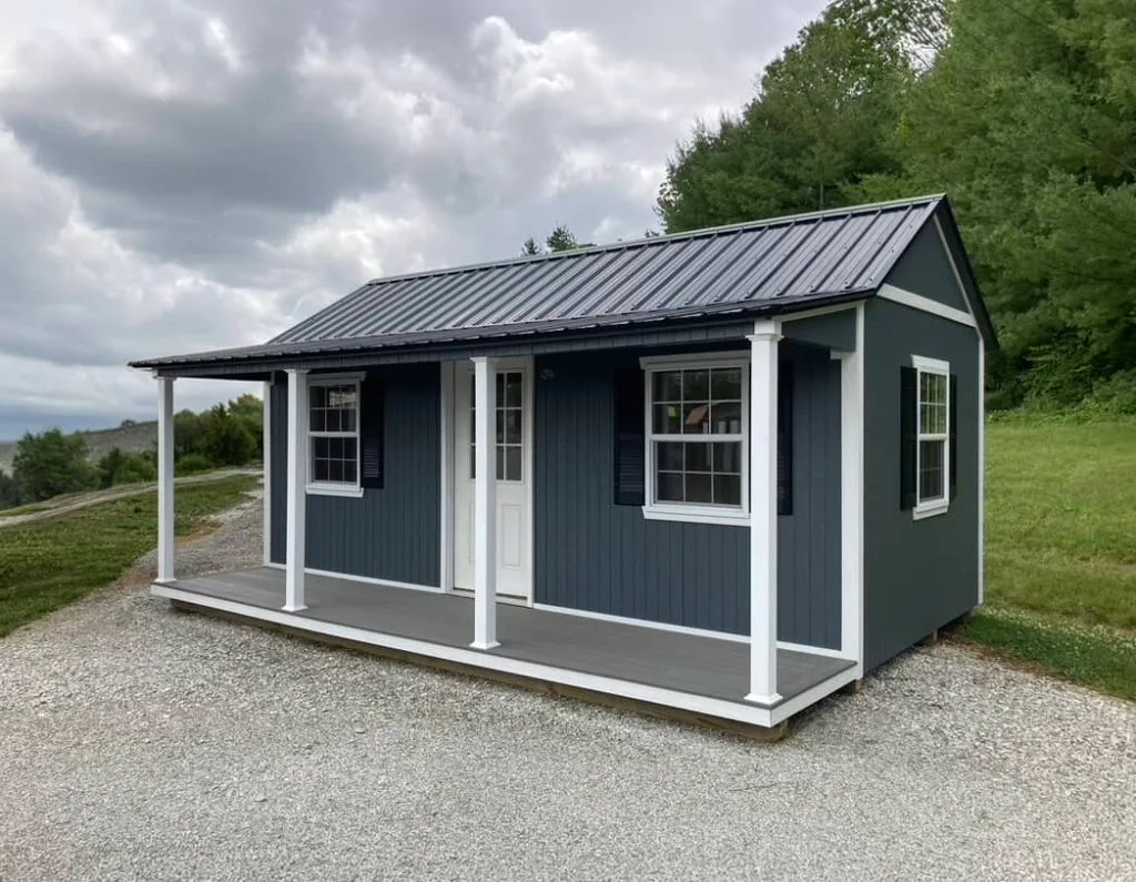 Blue Elite Pool House with white trim, covered front porch, and multiple windows on a gravel lot