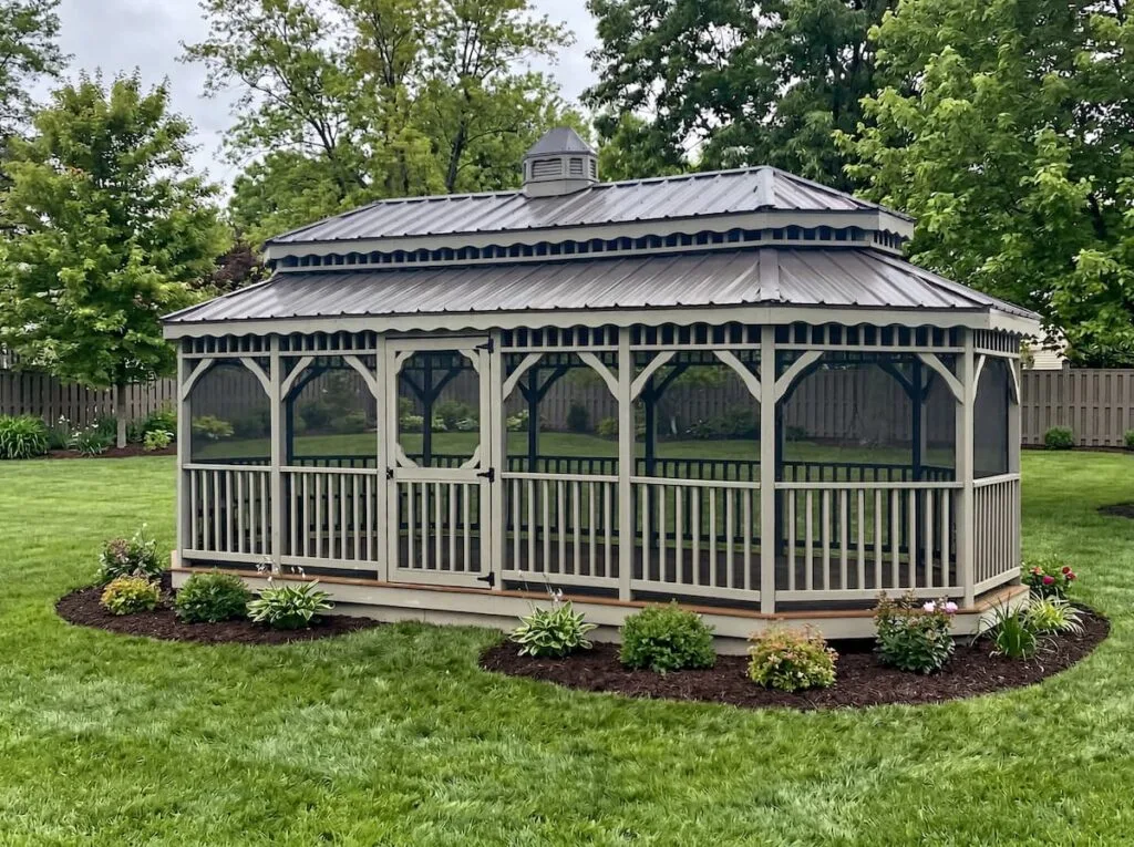 Oblong Gazebo with gray metal roof, screened sides, cupola, entry door, railing, and landscaped yard.