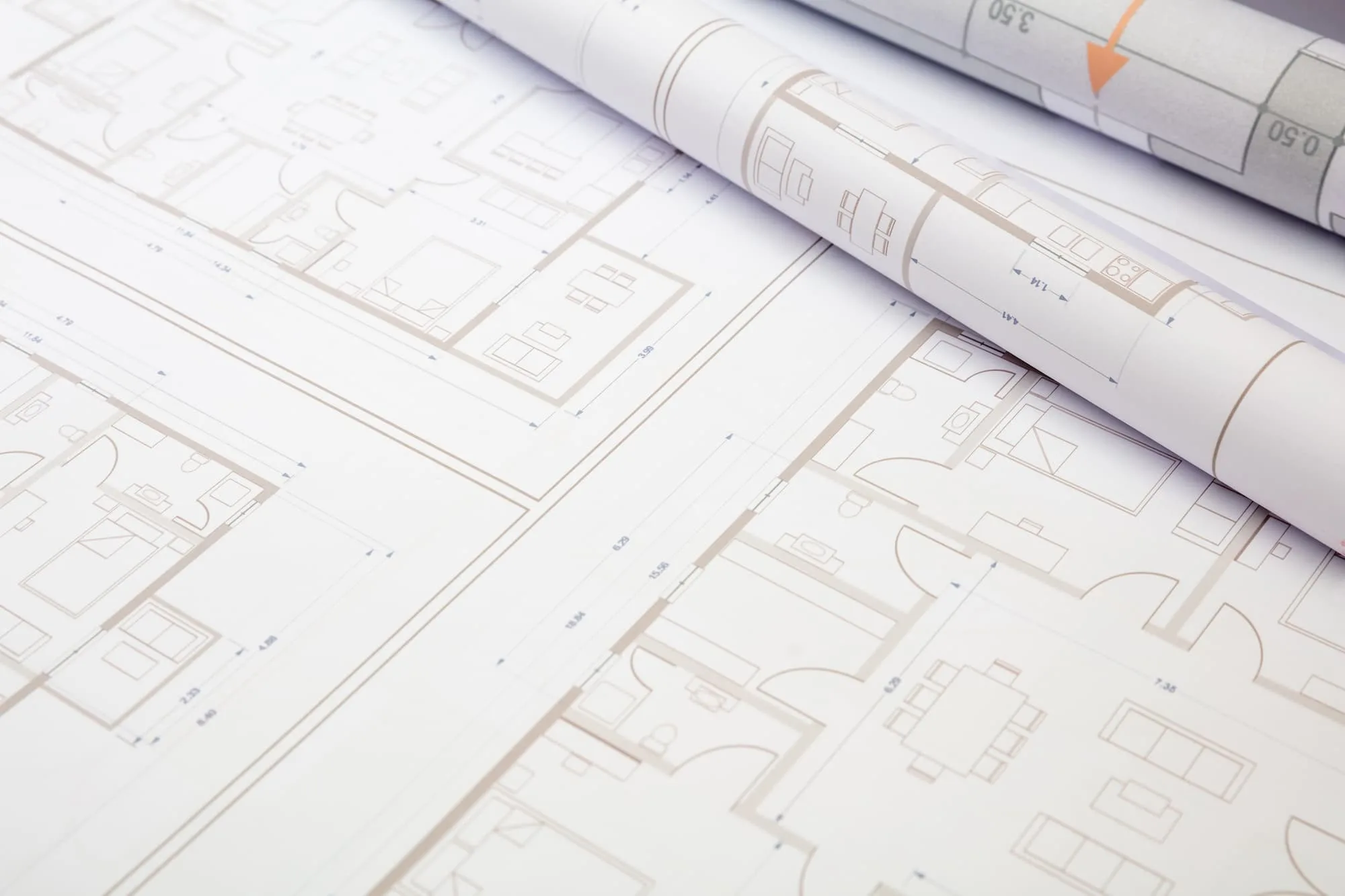 Rolled architectural blueprints resting on detailed floor plan drawings with room layouts and measurement markings.