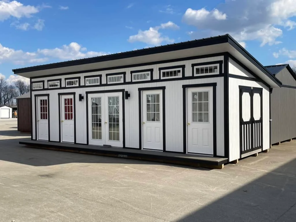 Extended white Elite She Shed Studio with black trim, multiple entry doors, center French doors, and a long row of clerestory windows.
